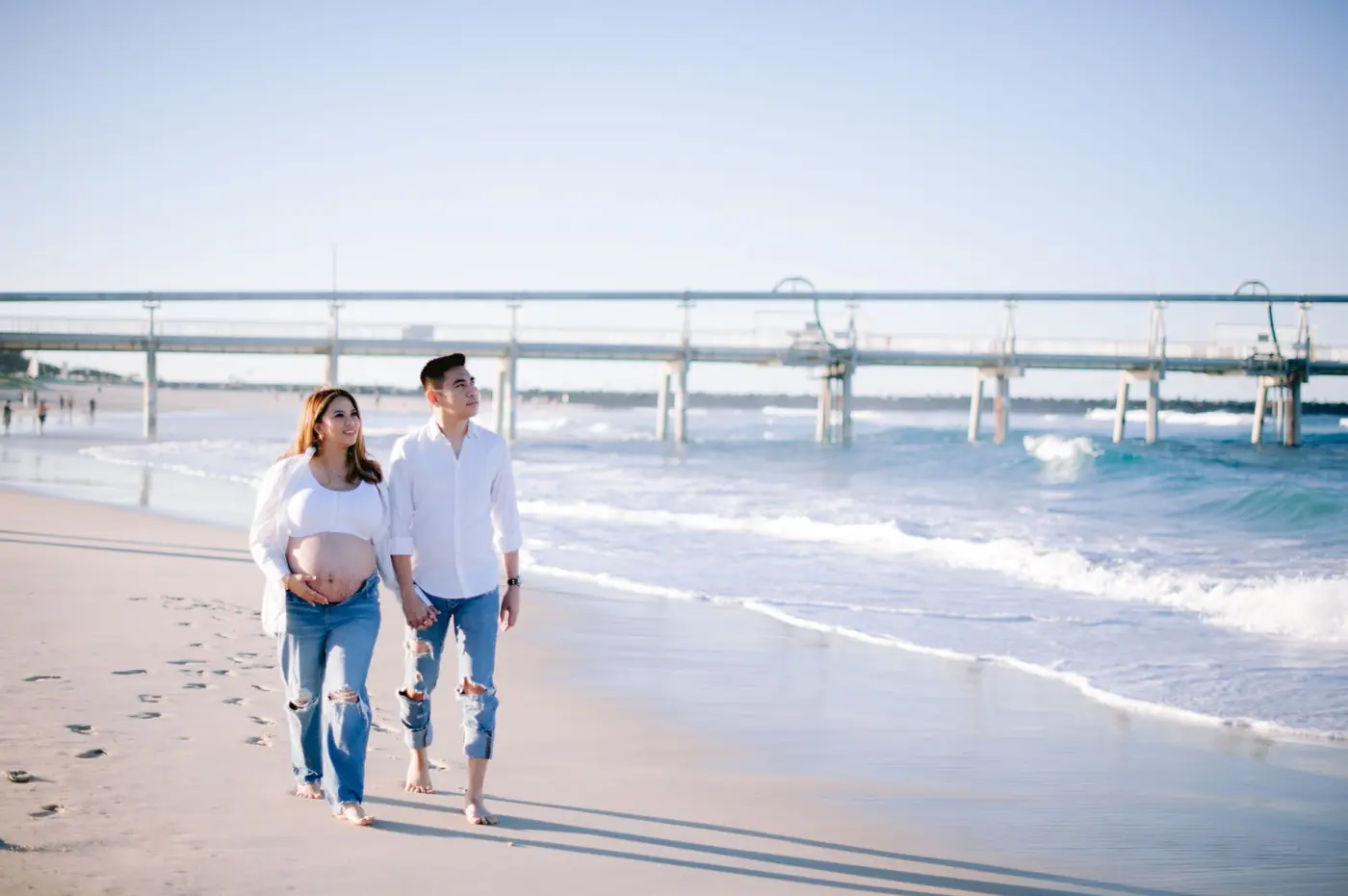 An expectant couple walking together along the beach at golden hour