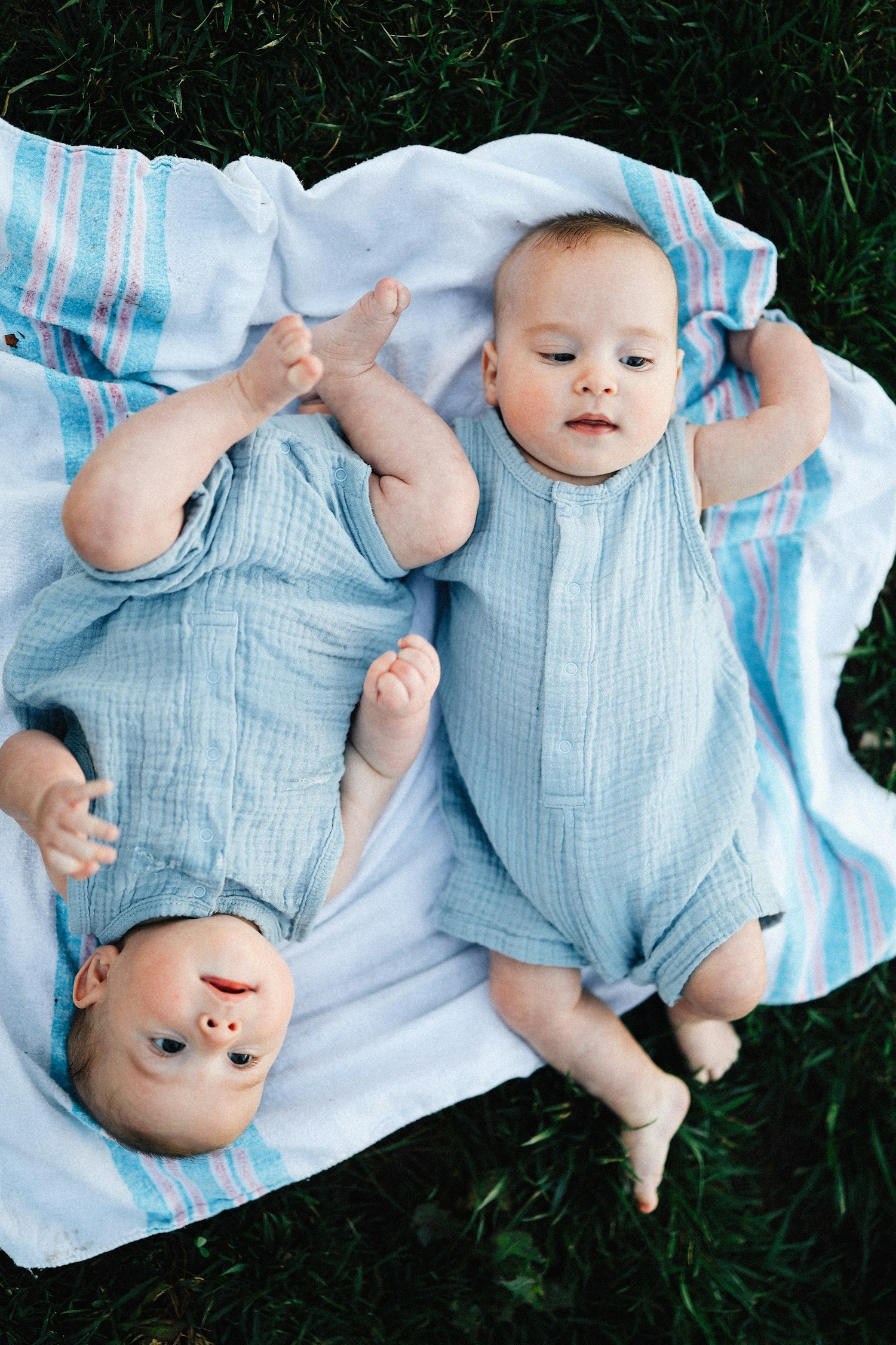 Twin babies lying happily side by side on a blanket